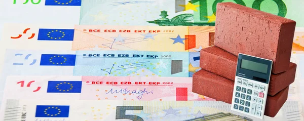 Dinero en efectivo en euros y ladrillos con calculadora de bolsillo como fondo — Foto de Stock