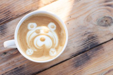 Ahşap bir masada bir kupa kahve. Ayı desenli kapuçino. Düz yatıyordu