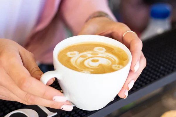 Barista girl serves ready-made latte coffee with drawn of a beautiful bear pattern