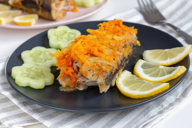 Havuçların altında, limonlu ve sebzeli siyah bir tabakta pişmiş beyaz balık. Yakın plan..