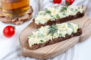 Yumurta soslu sandviçler (çavdar ekmeğine yumurta salatası) bir kupa çayla ahşap bir tahtada. Hızlı ve lezzetli kahvaltı yemekleri..