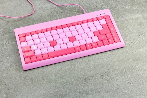 Modern, small, slim pink keyboard with thin keys on a grey cement background. Keyboard for a girl.