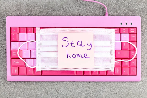 Pink keyboard on desktop with sticker. Stay home Stay safe. Concept of isolation and remote work.