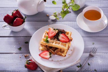 Beyaz arka planda çikolata soslu Belçika waffle tabağı ve taze çilek. Bir fincan çayla lezzetli tatlı.