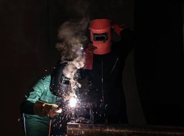 The welder is welding the steel with an electric welding machine inside the factory.