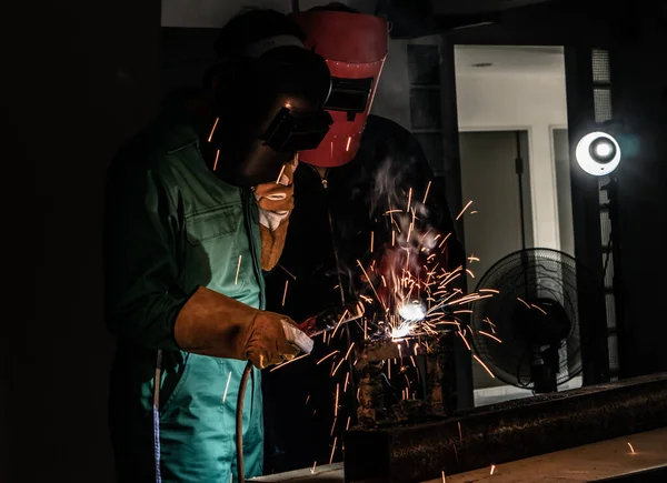 The welder is welding the steel with an electric welding machine inside the factory.