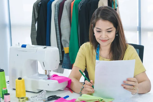 Asyalı bir kadın moda tasarımcısı mutlu bir şekilde çalışıyor. Küçük işletmeler evden çalışır..