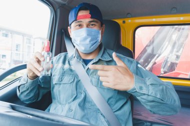 Toza ve gribe karşı korunmak için maske takan Asyalı kamyon şoförlerinin yakın plan fotoğrafları. Covid 19. Arabanın ön tarafında. Bir antiseptik taşıdı ve parmağını gösterdi..