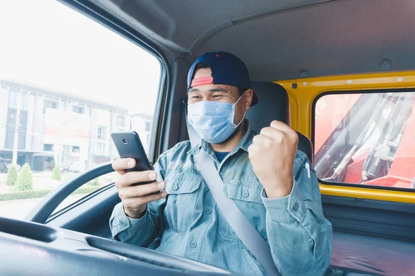 Toza ve gribe karşı korunmak için maske takan Asyalı kamyon şoförlerinin yakın plan fotoğrafları. Covid 19. Arabanın içinde. Akıllı telefon kullanıyor ve yumruğunu tutuyor..