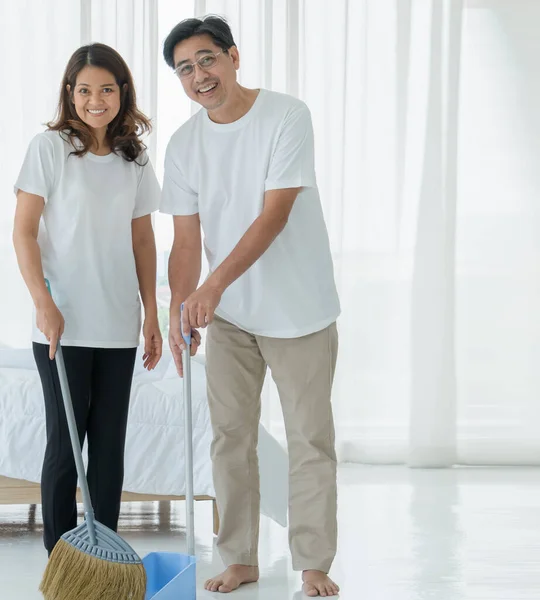 A senior Asian couple wearing white clothes is helping to clean the house happily and have fun on a refreshing holiday morning.