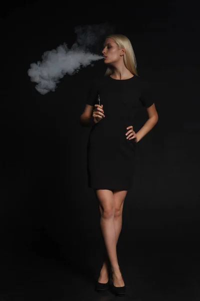 Femme en robe noire fume une cigarette électronique — Photo