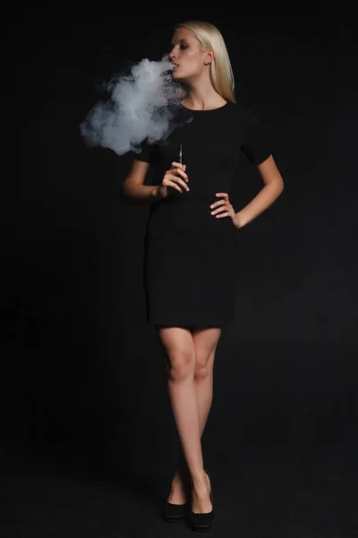 Mujer en un vestido negro fuma un cigarrillo electrónico — Foto de Stock