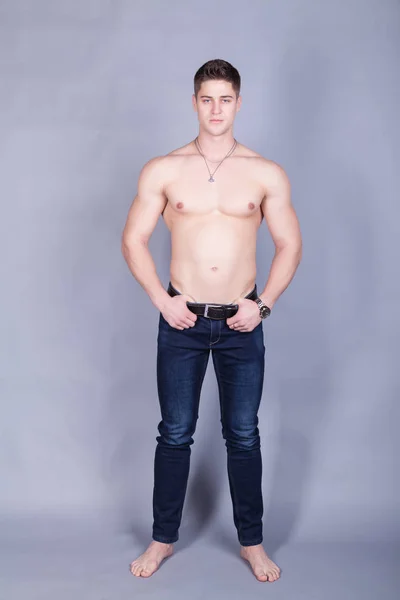 Joven con músculos de alivio en jeans con un torso desnudo sobre un fondo gris — Foto de Stock