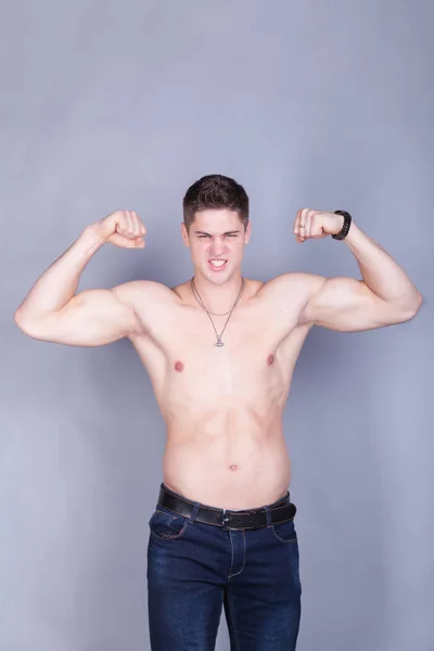 Jeune homme avec des muscles de soulagement en jeans avec un torse nu sur un fond gris — Photo