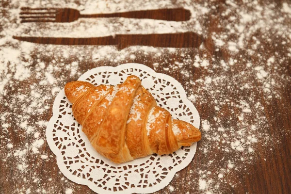 On wooden background croissant is sprinkled with cinnamon powder near — Stock Photo, Image