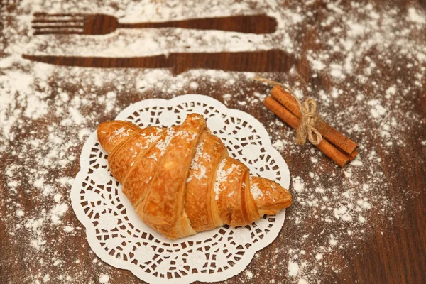 On wooden background croissant is sprinkled with cinnamon powder near — Stock Photo, Image