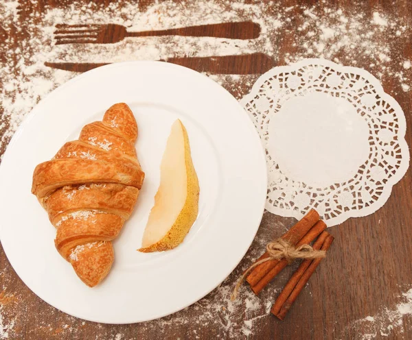 Birne und Croissant in Kokosraspeln sind ein hölzerner Hintergrund — Stockfoto