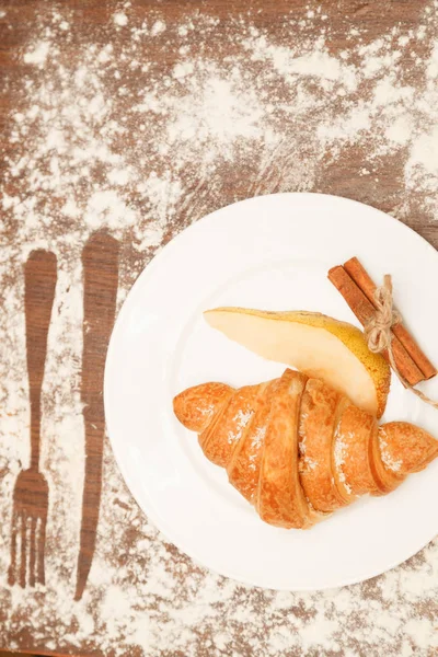 Pear and croissant in coconut chips are a wooden background — Stock Photo, Image