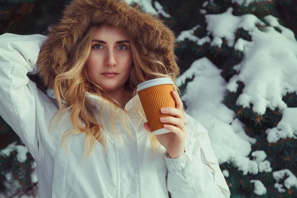 Young blond woman in a fur hood, holding a mug of coffee — Stock Photo, Image