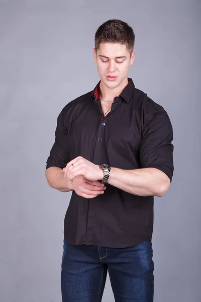 Pohledný mladý muž v černé košili s vyhrnutými, při pohledu na hodinky. — Stock fotografie