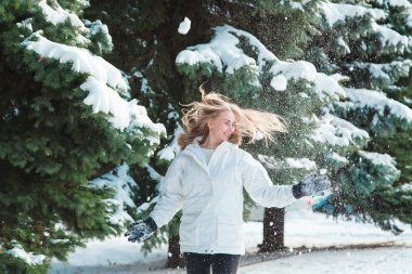 Soğuk bir kış günü genç güzel neşeli kadın beyaz ceketli uzun sarı saçlı kar ağaçlar karla kaplı zemin karşı oynadığı ve neşeyle gülüyor