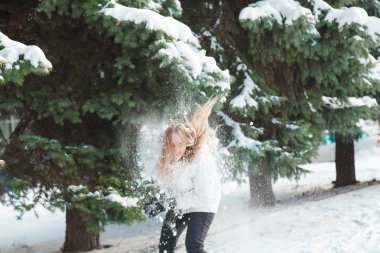 Soğuk bir kış günü genç güzel neşeli kadın beyaz ceketli uzun sarı saçlı kar ağaçlar karla kaplı zemin karşı oynadığı ve neşeyle gülüyor