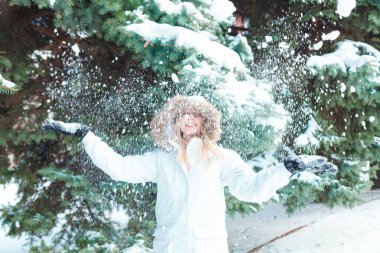Soğuk bir kış günü genç güzel neşeli kadın beyaz ceketli uzun sarı saçlı kar ağaçlar karla kaplı zemin karşı oynadığı ve neşeyle gülüyor