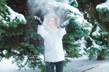 Soğuk bir kış günü genç güzel neşeli kadın beyaz ceketli uzun sarı saçlı kar ağaçlar karla kaplı zemin karşı oynadığı ve neşeyle gülüyor