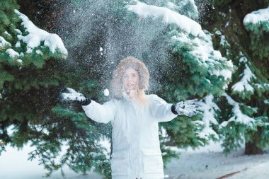 Soğuk bir kış günü genç güzel neşeli kadın beyaz ceketli uzun sarı saçlı kar ağaçlar karla kaplı zemin karşı oynadığı ve neşeyle gülüyor