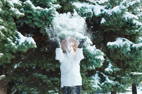 Soğuk bir kış günü genç güzel neşeli kadın beyaz ceketli uzun sarı saçlı kar ağaçlar karla kaplı zemin karşı oynadığı ve neşeyle gülüyor