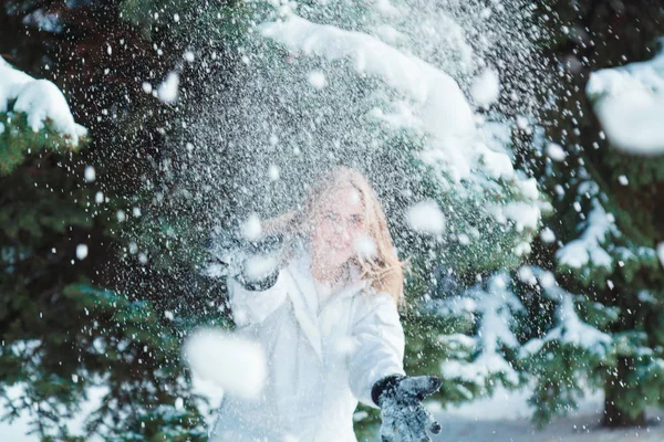 Soğuk bir kış günü genç güzel neşeli kadın beyaz ceketli uzun sarı saçlı kar ağaçlar karla kaplı zemin karşı oynadığı ve neşeyle gülüyor