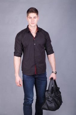 Stüdyo fotoğrafçılığı, büyük bir siyah çanta tutarak ellerinde siyah tişört ve kot giyen genç güçlü uzun boylu, yakışıklı adam