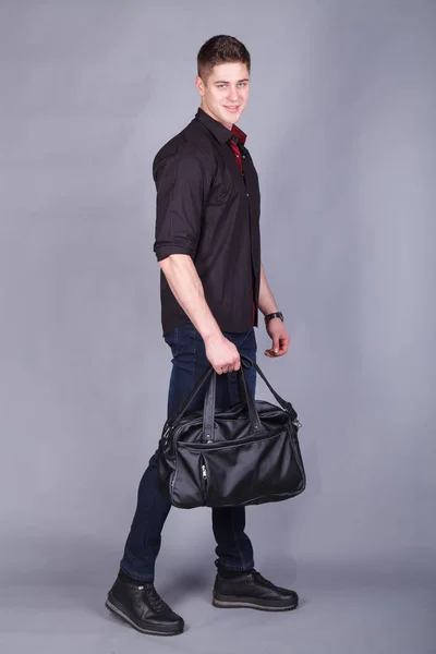 Photographie studio, jeune homme fort grand et beau portant une chemise noire et un jean bleu dans les mains tenant un grand sac noir — Photo