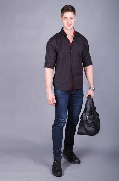 Photographie studio, jeune homme fort grand et beau portant une chemise noire et un jean bleu dans les mains tenant un grand sac noir — Photo
