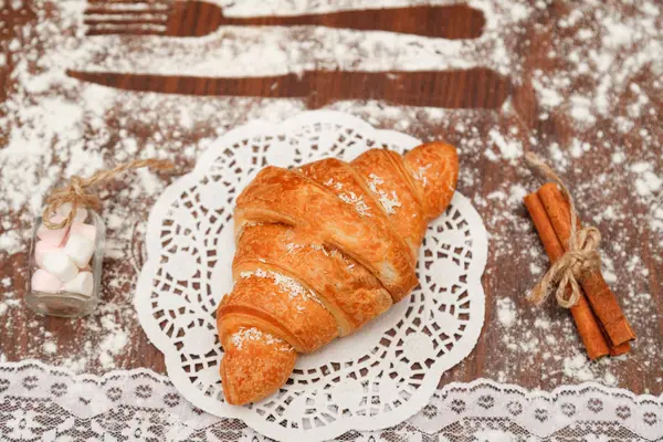 Auf einem Holzbrett liegt ein Croissant mit Schokolade unter dem weißen Tuch neben ihm Zimt, verschiedene Dekorationen, alle mit Mehl bemehlt. — Stockfoto