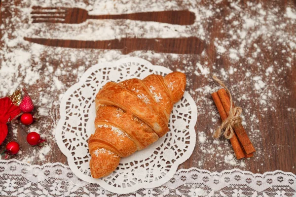 On a wooden board is a croissant with chocolate under the white cloth beside him cinnamon, various decorations, all floured. — Stock Photo, Image