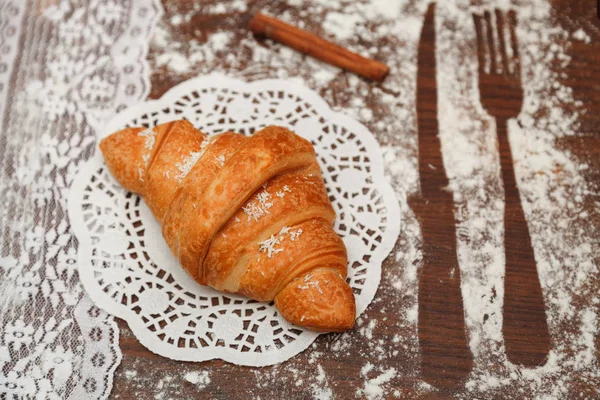 En una tabla de madera hay un croissant con chocolate debajo de la tela blanca a su lado canela, varias decoraciones, todo florado . — Foto de Stock