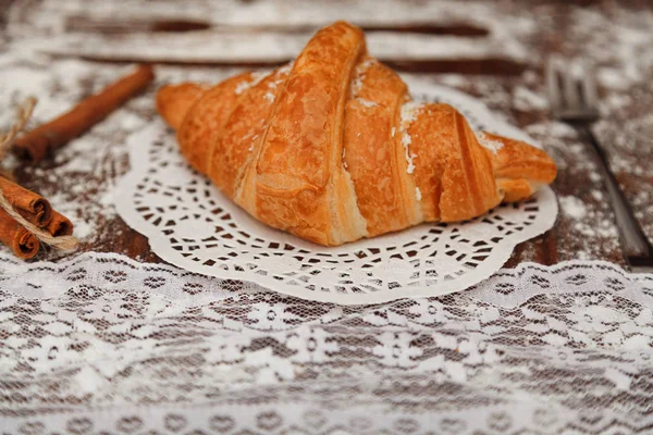 En una tabla de madera hay un croissant con chocolate debajo de la tela blanca a su lado canela, varias decoraciones, todo florado . — Foto de Stock