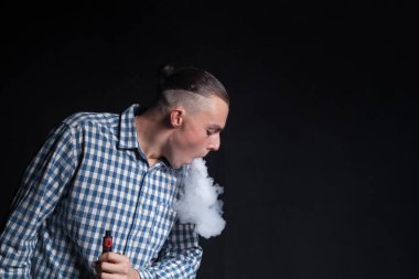 Mavi ekose gömlekli şık bir saç kesimi olan genç bir adam siyah bir zemin üzerine bir sigara elektronnuju içiyor. Egzoz sigara yapar duman halkaları rakamlar