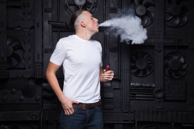 Bir adam beyaz bir T-shirt ve kot bir siyah arka plan vaping ve Buhar bulutu serbest bırakır.