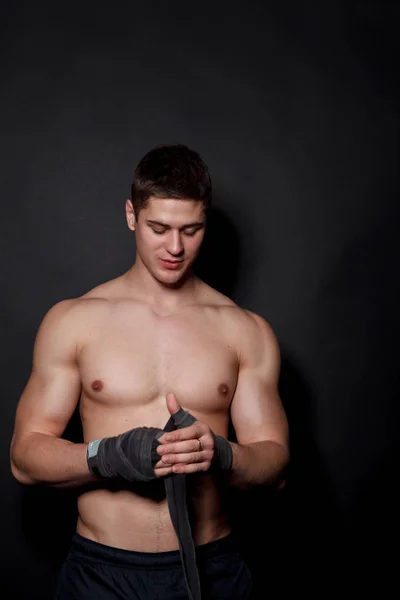 Sportowe bokser człowiek ściąga na okłady nadgarstka ręki. Kaukaski model mężczyzna na białym tle na ciemnym tle. — Zdjęcie stockowe