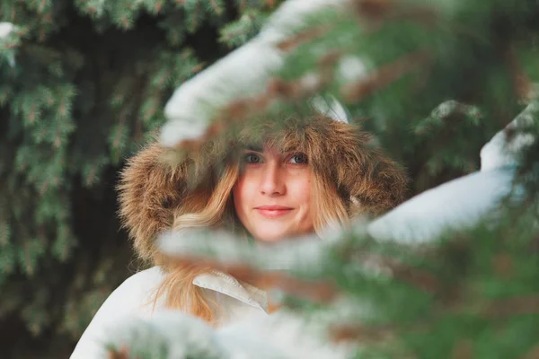 Junge, fröhliche Frau mit Kapuze und Fellspaß auf der Straße. im Winter kalter, sonniger Tag vor dem Hintergrund von Bäumen und Schnee. — Stockfoto