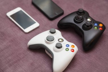 İki cep telefonları ve iki gamepad kanepede yalan. Beyaz ve siyah telefon ve beyaz ve joypad nintendo.