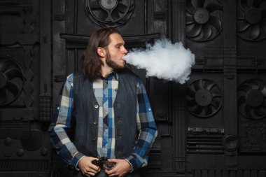 Sakal vaping siyah arka plan üzerine erkeklerle. Uzun saçlı genç adam elektronik sigara içiyor. 