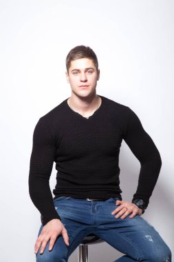 genç adam beyaz bir arka plan bir sandalyeye oturur. Siyah kazaklı bir adam.