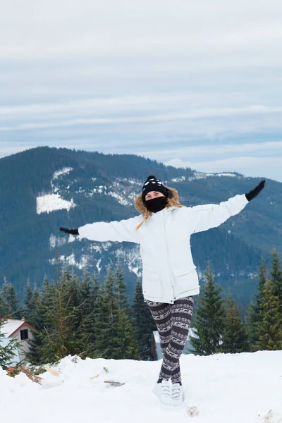 Glad ung kvinna stående på bakgrund av snöklädda berg. Flicka klädd i skidkläder — Stockfoto