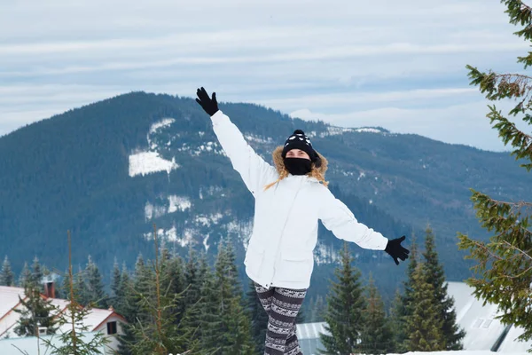 Glad ung kvinna stående på bakgrund av snöklädda berg. Flicka klädd i skidkläder — Stockfoto
