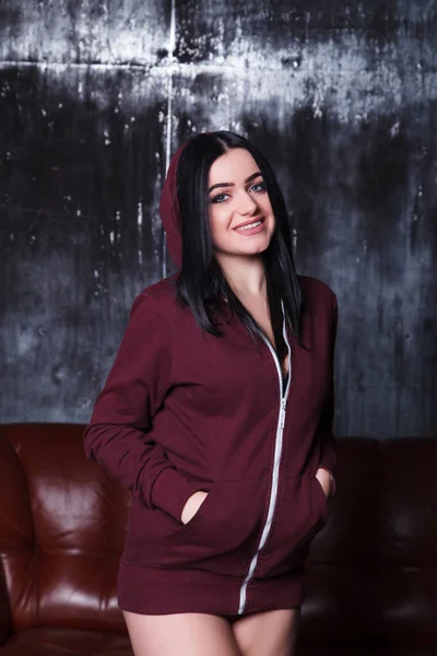 Funny sexy girl standing on the background of the sofa. Sexy woman in black lingerie and a burgundy sweatshirt — Stock Photo, Image