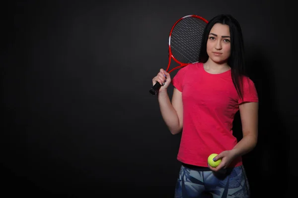 Esporte mulher em um fundo preto segurando uma raquete de tênis e bola — Fotografia de Stock