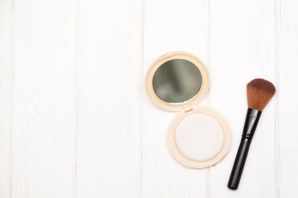 Brush and powder with a mirror on a white wooden background
